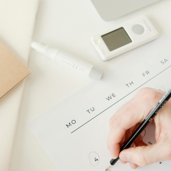 A person marking dates on a calendar, with a glucometer and laptop nearby, suggesting diabetes monitoring.